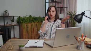 Genç kadın serbest çalışan, ofis masasında oturuyor cep telefonuyla müşteriye cevap veriyor, dizüstü bilgisayar kullanıyor. Sohbet. Yetişkin kız öğrenci eğitimi alıyor, uzaktan kumanda işinde çalışıyor, konuşuyor.