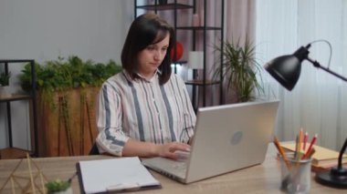 Young woman businesswoman sitting on desk closing PC laptop pc after finishing work at home office room. Girl freelancer working online, remote job. E-learning, browsing internet on notebook computer