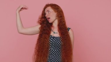 Dedikodular. Yalancılar! Kızıl saçlı genç bir kadın elleri, yuvarlanan gözleri, boş vaatleri, boş vaatleri olan saçma sapan jestler yapıyor. Kızıl çilli kız pembe arka planda kapalı yerde izole edilmiş.