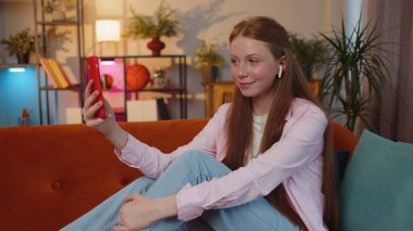 Genç, kızıl saçlı, kulaklık takan genç bir kız. Evde oturma odasındaki kanepede oturan aileyle telefonda sohbet ediyor. Zencefilli çocuk, hoparlörden keyif alıyor.