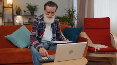 Gülümseyen, kıdemli büyükbaba muhasebe ödemeleri ve aylık harcamaları hesaplayan banka faturaları sınıftaki kanepede evrak analizi yapan. Dizüstü bilgisayarda çalışan yaşlı bir serbest yazar.