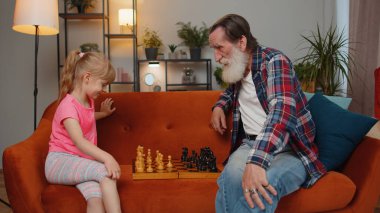 Gülümseyen büyük baba, evde genç torunuyla satranç oynuyor. Emekli büyükbaba, çocuk kızıyla kanepede dinlenerek masa oyunu oynuyor. Aile içi etkinlik