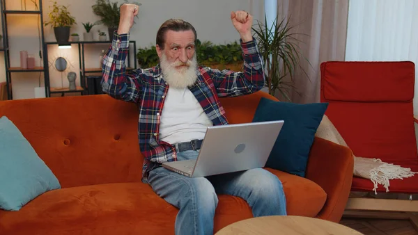 Веселый Старший Дедушка Домашнем Диване Ноутбуком Кричать Восторге Поднять Руки — стоковое фото