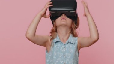 Young preteen child girl kid using virtual reality futuristic technology VR app headset helmet to play simulation 3D 360 video game, watching film movie. Little toddler children on pink background