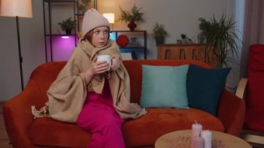 Hasta çocuk, ekoseye sarılı şapka takıyor. Kanepede soğuktan titriyor. Isıtılmamış bir dairede sıcak çay içiyor. Sağlıksız çocuk kendini kötü hissediyor, ısınmaya çalışıyor.