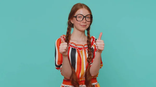 Great nice job. Cheerful positive happy girl in dress showing thumbs up and nodding in approval, successful good work. Young stylish ginger teenager child on blue background. People sincere emotions