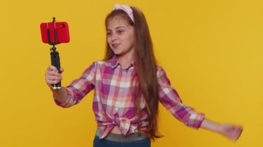 Genç kız çocuk blogcu kız akıllı telefon özçekim çubuğuyla selfie çekiyor abonelerle internet üzerinden video görüşmesi yapıyor. Stüdyo sarı arka planda izole edilmiş küçük çocuklar.