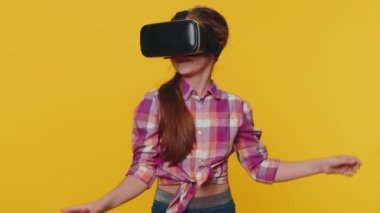 Young preteen child girl kid using virtual reality futuristic technology VR app headset helmet to play simulation 3D 360 video game, watching film movie. Little toddler children on yellow background