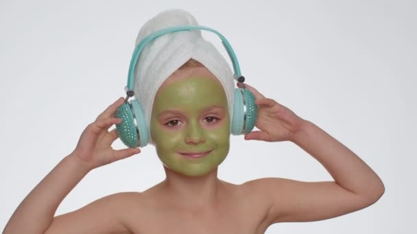 Uśmiechnięta Dziewczynka Kąpieli Ręczniku Głowie Nawilżająca Zielona Maska Twarzy Słuchająca — Wideo stockowe