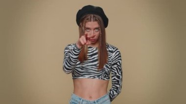 I am watching you. Lovely pretty young woman pointing at her eyes and camera, show I am watching you gesture, spying on someone. Adult stylish girl isolated alone on beige studio background indoors
