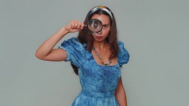 Araştırmacı bilim adamı kadın, elinde büyüteçle kameraya bakıyor, yakından bakıyor, araştırıyor, analiz ediyor. Gri stüdyo arka planında yetişkin tarzı bir kız.