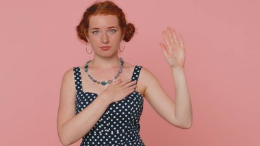 Dürüst olacağıma yemin ederim. Saygıdeğer kızıl saçlı kadın yemin etmek için elini kaldırıyor. Dürüst olacağına ve elini göğsüne koyduğunda doğruyu söyleyeceğine söz veriyor. Pembe arka planda çilli kızıl kız.