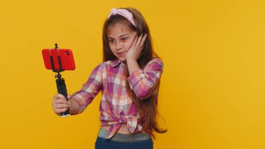 Wow reaction. Impressed young preteen child girl kid blogger taking selfie on mobile phone selfie stick, communicating video call online. Little toddler children isolated on studio yellow background