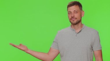 Bearded handsome young man showing thumbs up and pointing left empty place, advertising area for commercial text, copy space for goods promotion. Adult guy isolated on chroma key studio background