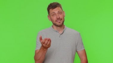 Need some more, please give me. Bearded young man showing a little bit gesture with sceptic smile, showing minimum sign, measuring small size. Adult guy isolated on green chroma key studio background