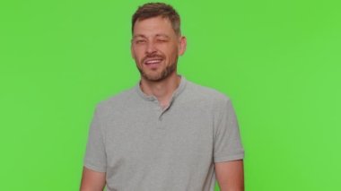 Gülümseyen mutlu adam göz kırpıyor, kameraya dişlek bir gülümsemeyle bakıyor, göz kırpıyor ve flört ediyor, iyimserliğini ifade ediyor. Yetişkin erkek adam yeşil krom anahtar stüdyo arka planında tek başına kapalı.