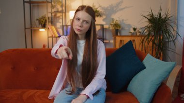 Hey sen! Genç kızıl saçlı kız heyecanlı bir şekilde gülümsüyor ve kamerayı işaret ediyor, şanslı kazananı seçiyor, muhteşem olduğunu gösteriyor, davet ediyor, onaylıyor. Evde oturan çilli çocuk kanepede oturuyor.