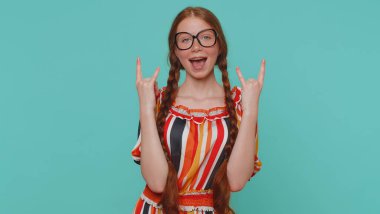 Rock n roll. Aşırı neşeli kızıl saçlı kız el hareketi yapıyor, havalı bir işaret veriyor, evet diye bağırıyor çılgın bir ifadeyle, dans ediyor, duygusal olarak başarıyla seviniyor mavi arka planda tek başına kazanıyor.