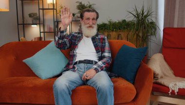 Yaşlı büyükbaba kameraya dostça gülümsüyor ve el sallıyor merhaba, merhaba, merhaba ya da güle güle, misafirperver bir yüz ifadesiyle karşılıyor. Yaşlı emekliler evlerinde, odalarında kanepede.