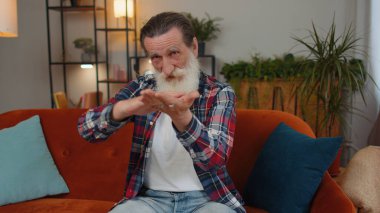 Neşeli, yaşlı, yaşlı ve yaşlı bir adam el hareketini boşa harcıyor ya da etrafa para saçıyor. Daha fazla bahşiş, daha fazla kazanç, piyango, vücut dili, paylaşım. Evde, kanepede oturan yaşlı bir adam.