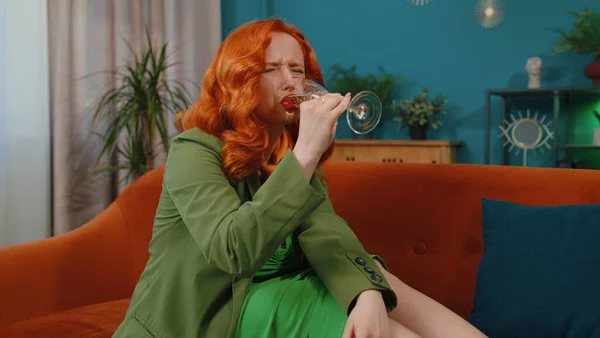Sad young redhead woman sitting at home looks pensive of unrequited love, suffers from unfair situation, drinking champagne. Girl problems, break up, depressed feeling bad annoyed, burnout, bankruptcy