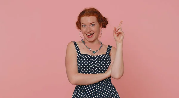 Eureka. Inspired young woman pointing finger up with open mouth, having good idea, plan, startup, showing inspiration motivation gesture, problem solution. Ginger freckles girl on pink wall background