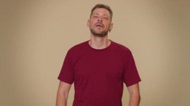 Time out, need a break. Tired serious upset handsome young man in red t-shirt showing pause relax gesture, limit or stop sign. Adult stylish male guy isolated alone on beige studio background indoors