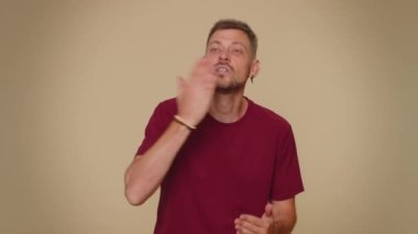 Smiling romantic handsome young man sending lots of air kisses looking at camera and smiling, missing you, love confession. Bearded stylish male guy isolated alone on beige studio background indoors