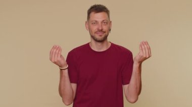 Bearded handsome young man showing wasting or throwing money around hand gesture, more tips dreaming about big profit body language. Adult stylish male guy isolated on beige studio background indoor