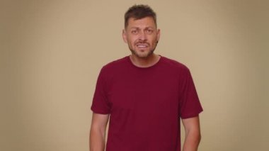 I cant hear you. What. Young man trying hear you, looking confused and frowning, keeping arm near ear for louder voice, asking to repeat, to hear information, deafness. One guy on beige background