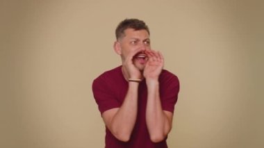 Expressive bearded handsome young man holding hands near mouth loudly screaming, shouting, yelling, announces discounts sale Hurry up, welcomes someone hello. Adult stylish guy on beige background