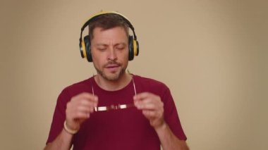 Happy handsome relaxed man with purple coiffure hairstyle listening music via headphones and dancing disco fooling around having fun expressive gesticulating hands. Adult stylish male guy indoors