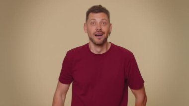 Happy handsome young man shouting, raising fists in gesture I did it, celebrating success, winning, birthday, lottery goal achievemen. Adult stylish guy isolated on beige studio background indoors