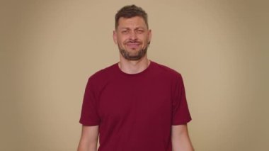 Upset bearded handsome young man showing thumbs down sign gesture, expressing discontent, disapproval, dissatisfied, dislike. Adult stylish male guy isolated alone on beige studio background indoors