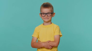 Sarı tişörtlü, gülümseyen, kameraya bakan, başarının tadını çıkaran, sürpriz yapan neşeli, komik, küçük çocuk. Gözlüklü anaokulu çocuğu mavi stüdyo arka planında tek başına. Çocukluk