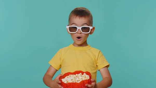 小孩子穿着T恤吃爆米花 戴着3D眼镜看喜剧电影 喜欢看电影小吃 戴眼镜的学龄前幼儿孤身一人 背景是蓝色的 — 图库照片