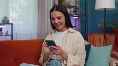 Oh my God Wow. Excited happy joyful winner girl use smartphone typing browsing found out great win good news celebrate victory. Young woman with mobile phone lying at home in room on orange couch