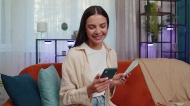 Planning family budget. Smiling caucasian girl counting money cash, use smartphone calculate domestic bills at home. Joyful young woman satisfied of income and saves money for planned vacation, gifts