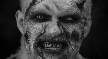 Kanlı yara izleri ve Cadılar Bayramı stili zombi makyajlı ürkütücü bir adam. Korkunç yaralı ölümsüz adam burnundan duman üflüyor, korkunç bir şekilde gülümsüyor. Voodoo ayinleri. Şeytani canavar, canavar, vampir