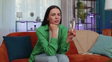 Sad young woman looks pensive of unrequited love, suffers from unfair situation, drinking champagne. Problem, break up, depressed feeling bad annoyed, burnout, bankruptcy. Girl sitting at home room