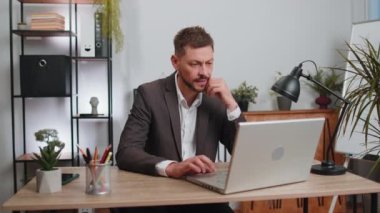 Concentrated businessman winner in suit working on laptop at home office desk typing browsing say Wow yes found out great big lottery win good news celebrate. Male manager freelancer man occupation