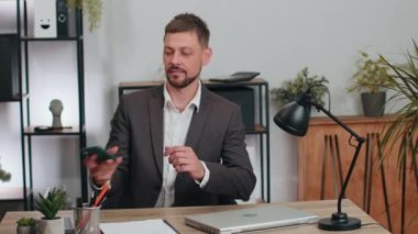 Businessman in suit entering office room working on smartphone, doing manager job, typing message to client. Confident serious male manager freelancer man busy occupation sitting at desk with laptop