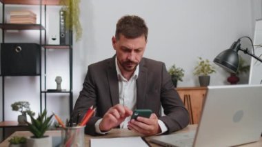 Businessman programmer software developer in suit working, making online purchase payment shopping with credit bank card and smartphone at modern office desk with laptop. Male freelancer business man