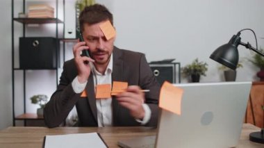Tired exhausted businessman in suit working on laptop at office with many sticker task inscriptions. Freelancer man busy occupation feels sad boredom overworked multitasking. Panic attack, deadline