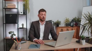 Businessman in suit working on laptop computer, meditating, doing yoga breathing exercise in lotus position at home office desk. Calm serene freelancer man taking break. Busy occupation. Peace of mind