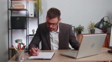 Stressed man feeling worried about problem analyzing information, read business papers prepare financial report at office. Male freelancer man frustrated thinking of money debt, budget loss bankruptcy