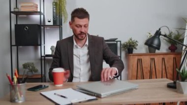 Businessman freelancer enters office start working on laptop computer at desk and drinking morning coffee. Man works on notebook, sends messages makes online purchases watching social media movies