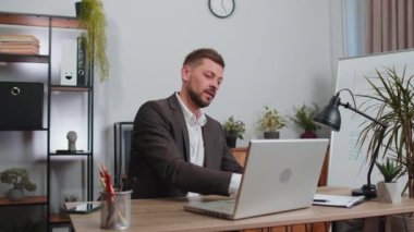 Happy relaxed overjoyed businessman in suit working on laptop computer at office wearing earphones listening favorite energetic disco music on smartphone. Male freelancer man relaxing, taking a break