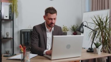 Joyful businessman in suit working on laptop computer sincerely rejoicing win, receiving money dollar cash banknotes, success lottery luck at office workplace desk. Professional manager freelancer man