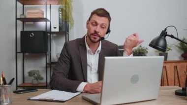 Businessman working on laptop computer wearing headset, freelance worker call center or support service operator helpline, having pleasant talk with client or colleague communication support at office